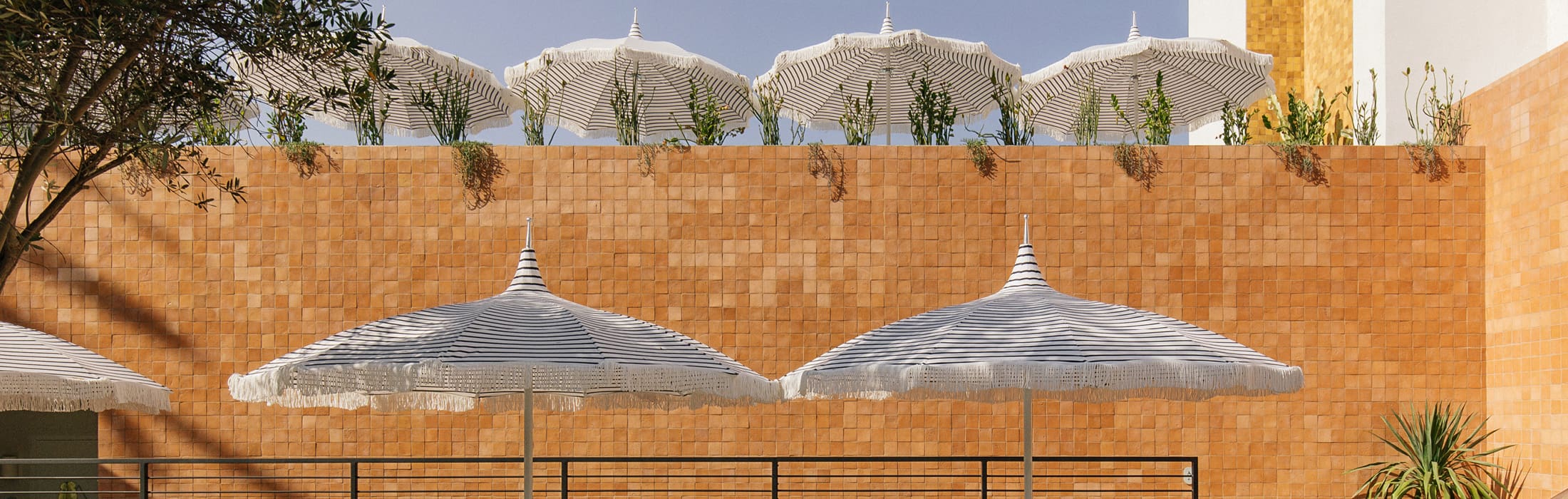 Pin-striped parasols framed by potted plants and an orange tiled wall at Silver Lake Pool & Inn