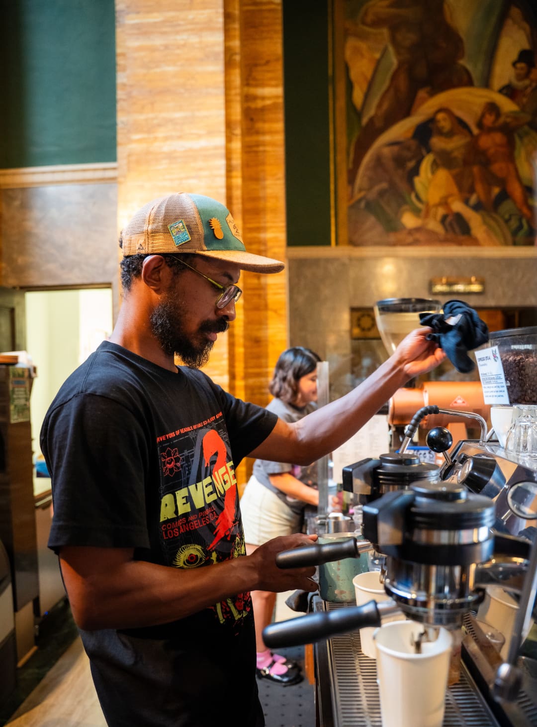 A man pouring coffee at Aquarela by a Hugo Ballin mural