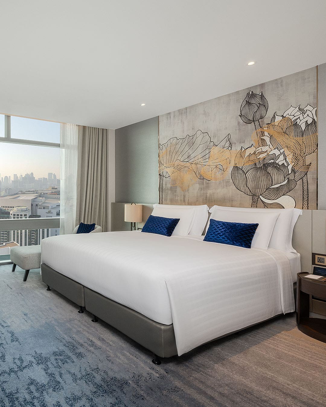 View of Executive Suite with king size bed and artwork on wall, window out on Bangkok with buildings behind