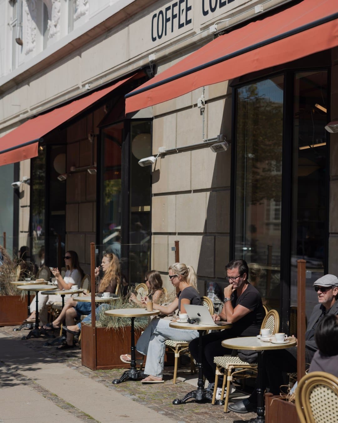 People beneath red awnings at tables outside Coffee Collective Trianglen
