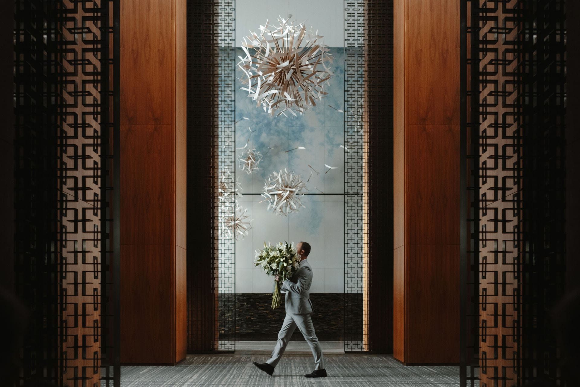 An employee at the Four Season walks through the lobby holding a large bunch of flowers. He is framed in an appealing way