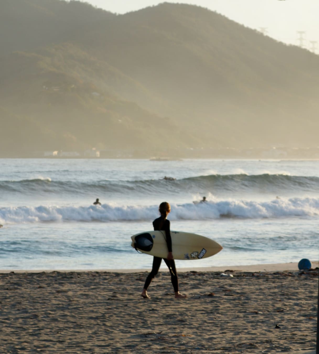 A surfer on a beach in Fukui with mountains behind.