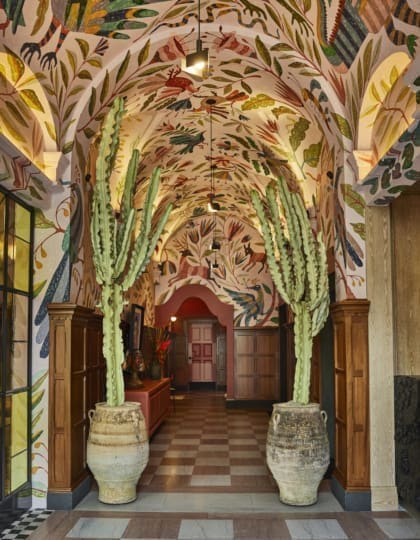 Best places to stay in LA | The entrance inside Downtown LA Hotel, where two tall cactuses in worn terracotta pots flank an arched corridor, with colourful modern frescoes painted on the ceilings