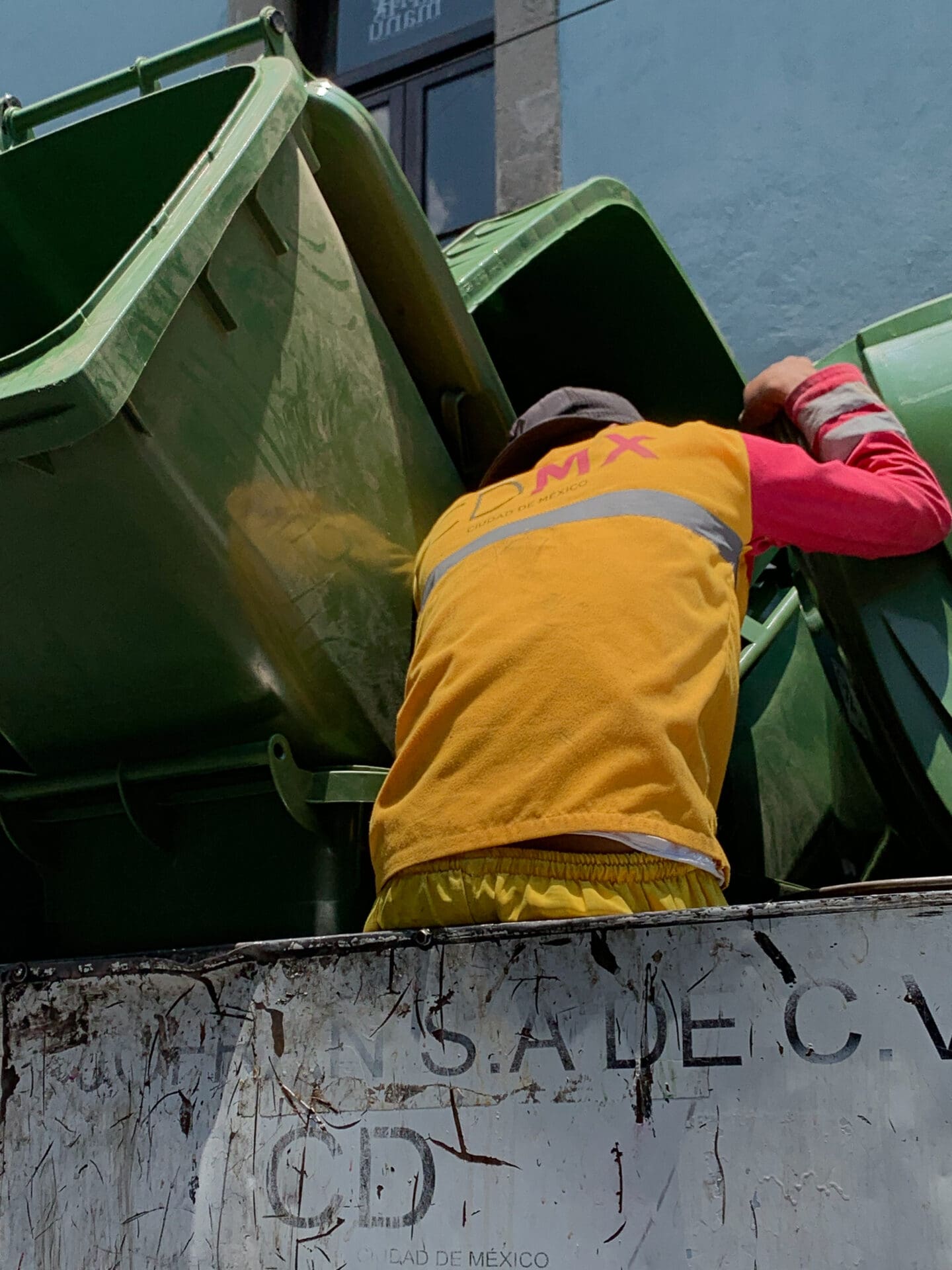 Photographer Manuel Zúñiga on Mexico City | A worker wearing a yellow jacket with red sleeves holds green wheelie bins