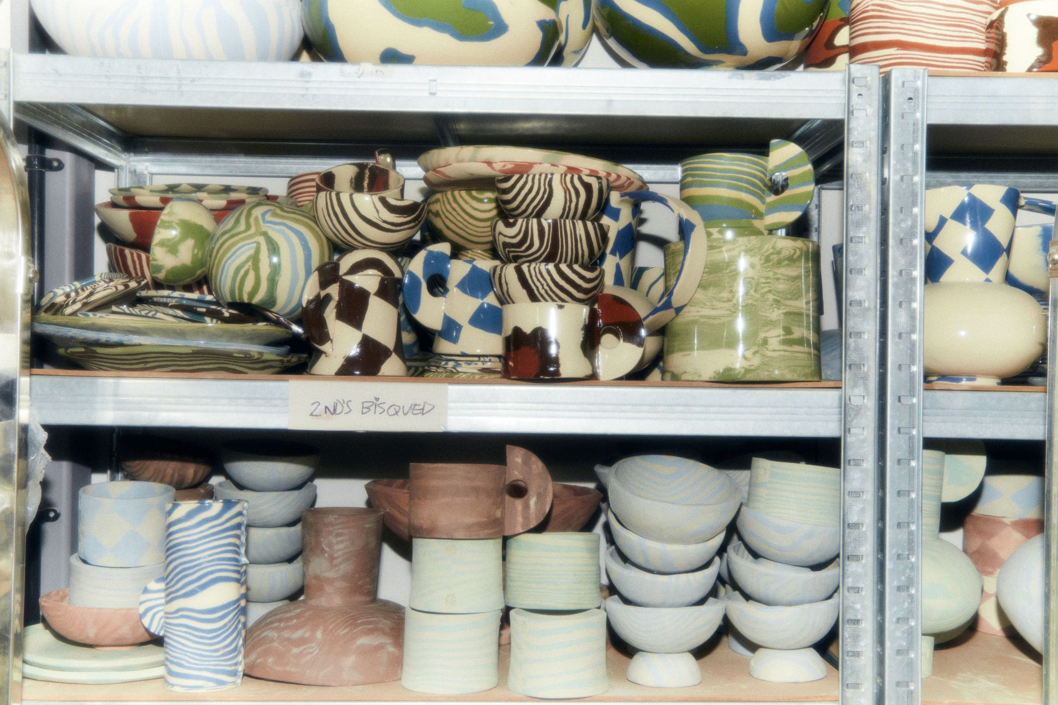 In the studio with Henry Holland | An assortment of bowls, cups, plates and mugs on shelves at various stages of firing.