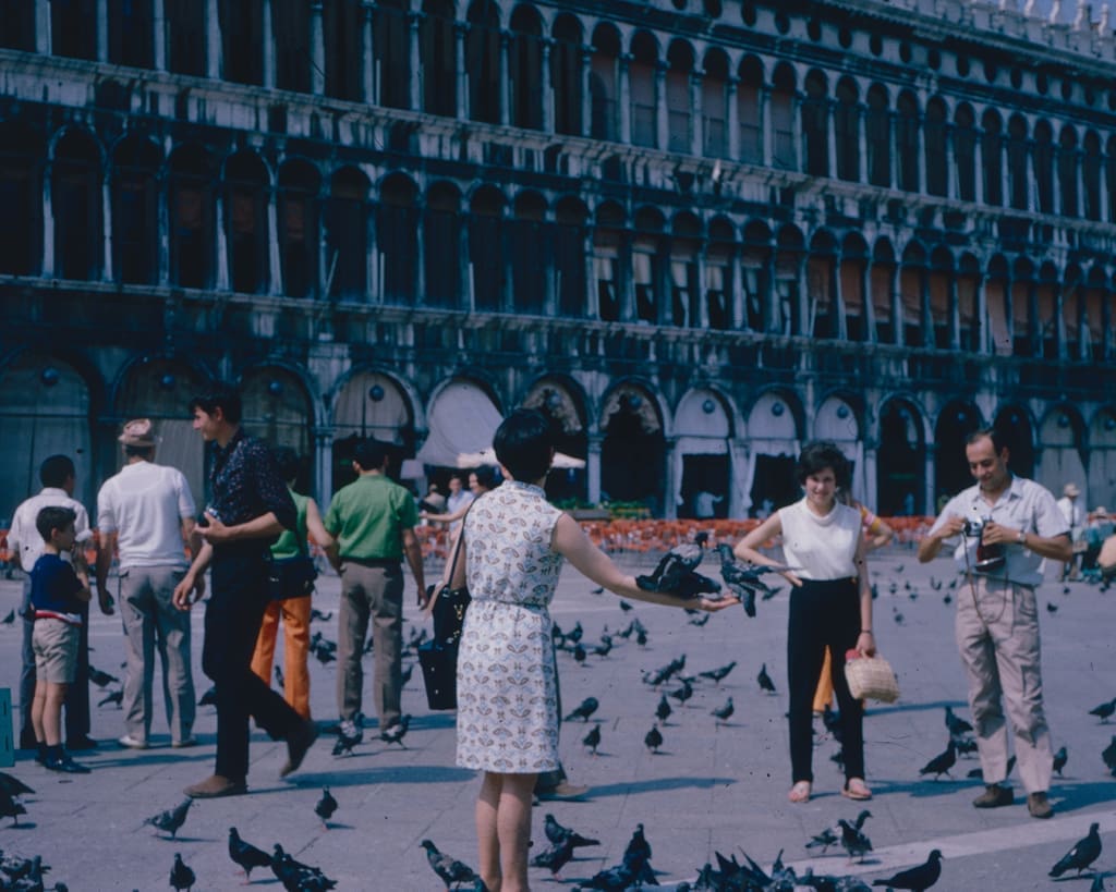 A group of tourists in Venice dancing next to pigeons, circa 1960